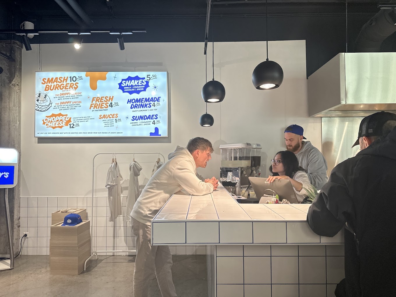 The interior of halal restaurant Drippy's in Rotterdam, Netherlands, showing a modern counter with a menu board, staff interacting with customers, and a clean, minimalist design.