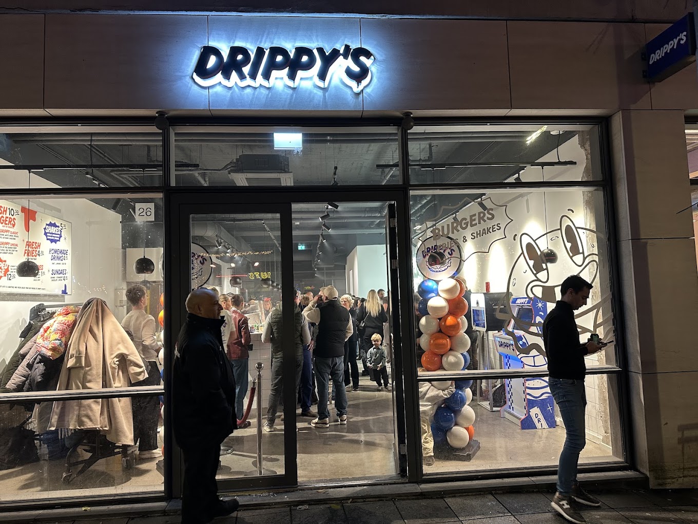 The exterior of halal restaurant Drippy's in Rotterdam, Netherlands, showing a modern storefront with a lit sign, large windows, and a crowd of people inside.