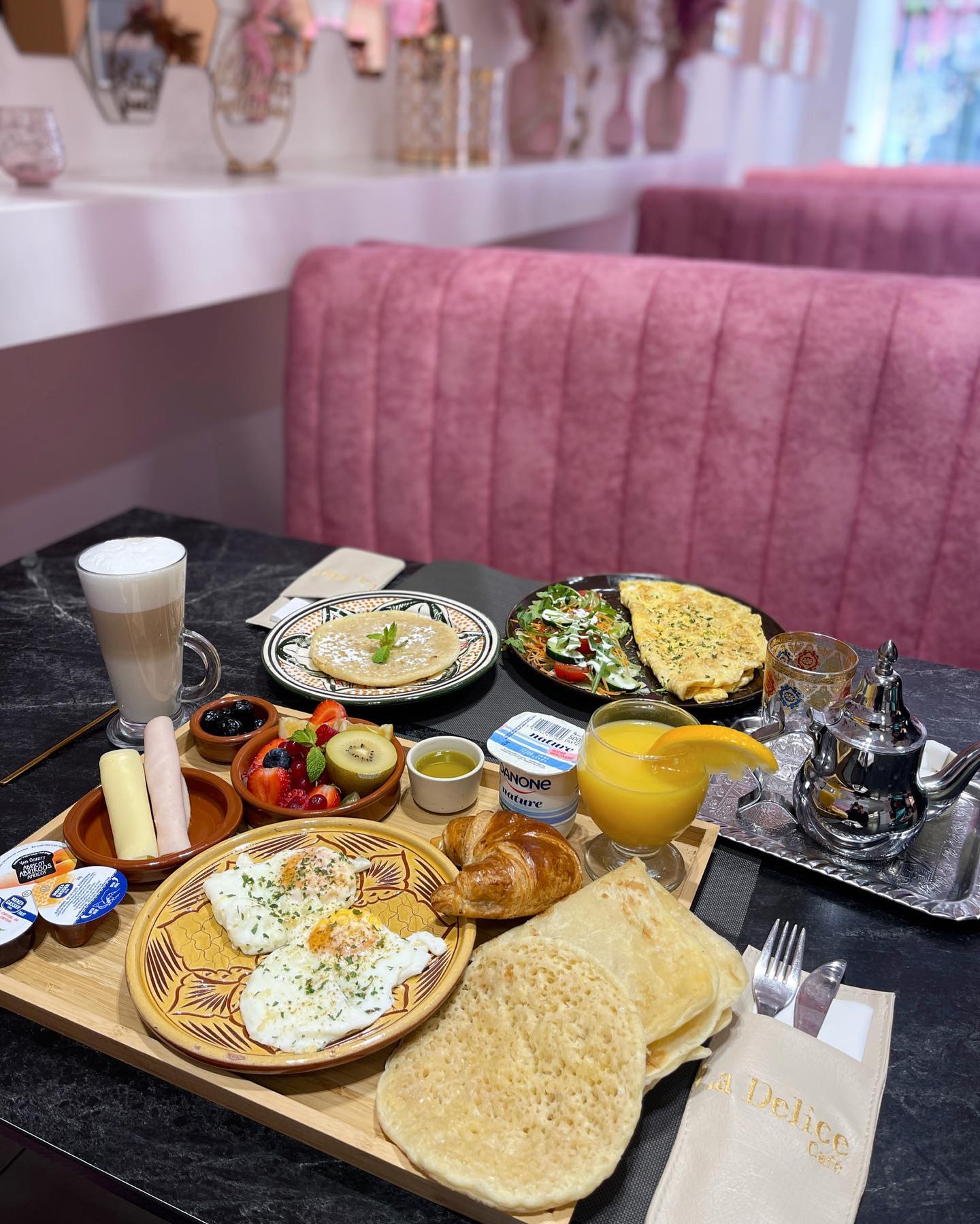 A breakfast platter featuring eggs, croissant, fresh fruits, pancakes, and drinks at La Delicé Café, a halal restaurant in Mechelen, Belgium.
