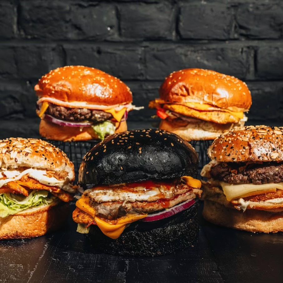 A variety of burgers including a black bun burger with chicken and cheese, and other burgers with sesame seed buns at Le Passage, a halal restaurant in Molenbeek-Saint-Jean, Belgium.