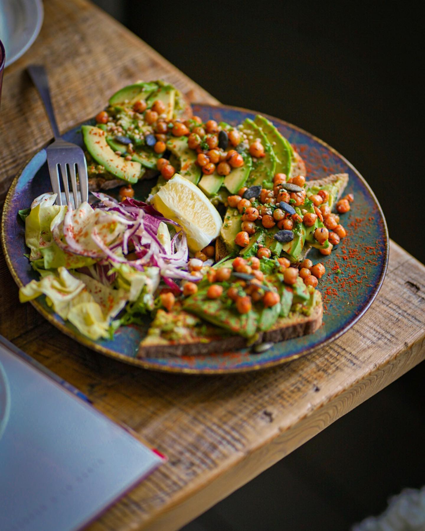 A plate of avocado toast topped with chickpeas, served with a side salad and lemon at La Table Rustique, a halal restaurant in Bruxelles, Belgium.