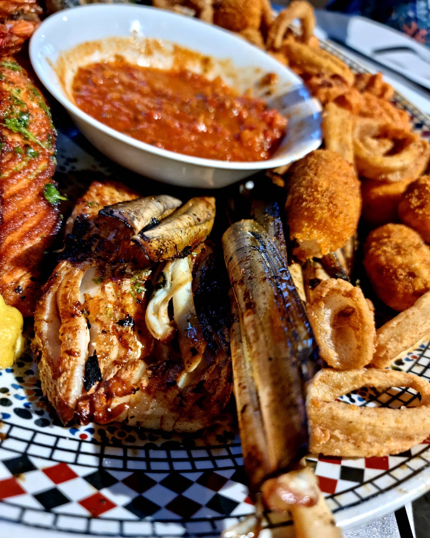 A platter of grilled seafood including fish, calamari, and a spicy dipping sauce at Zeester Eindhoven, a halal restaurant in Eindhoven, Netherlands.