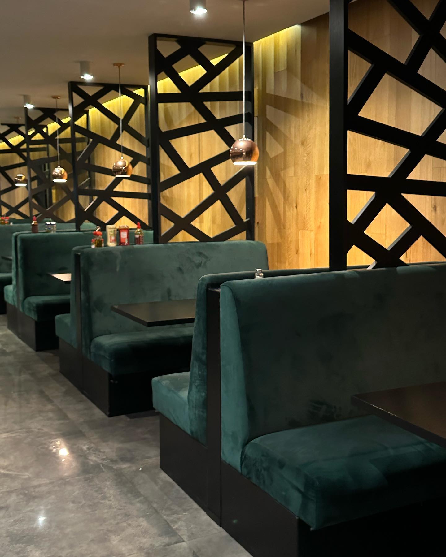 Het interieur van halal restaurant Wyngs in Schaerbeek, België, met groene fluwelen banken, zwarte tafels en decoratieve houten panelen met geometrische patronen.
