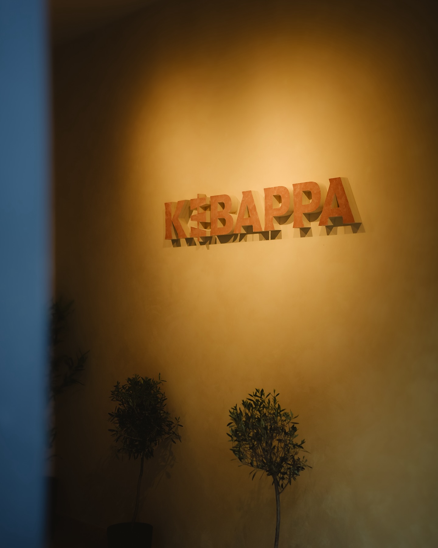 The interior of halal restaurant Kebappa in Schaerbeek, Belgium, showing a warm wall with the restaurant's name in bold letters and small potted plants.