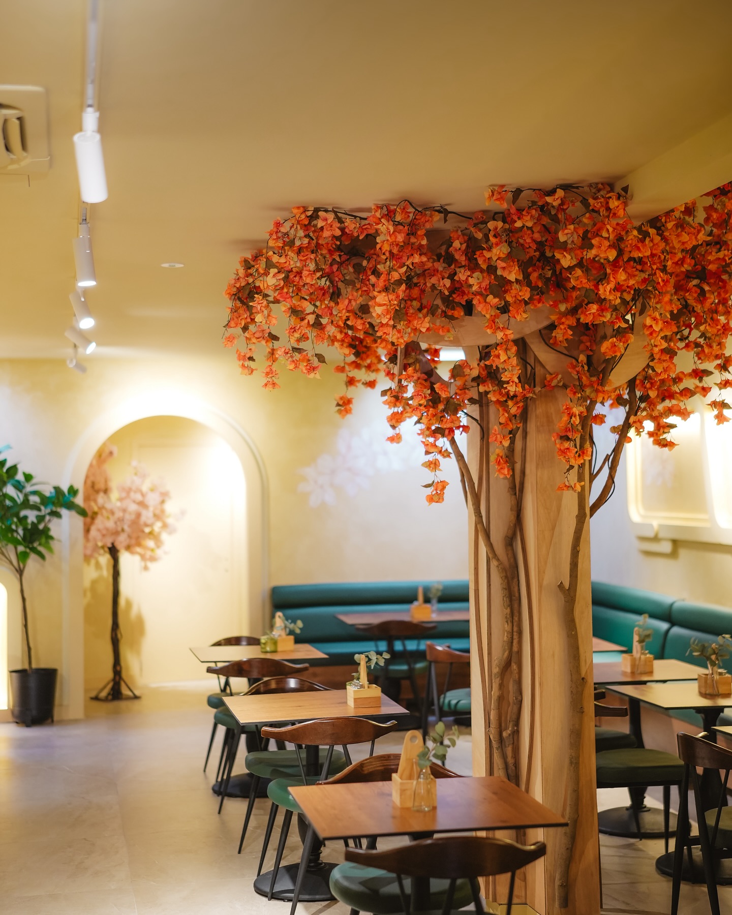 The interior of halal restaurant Kebappa in Schaerbeek, Belgium, showing wooden tables, green chairs, and decorative orange flowers on a tree-like structure.