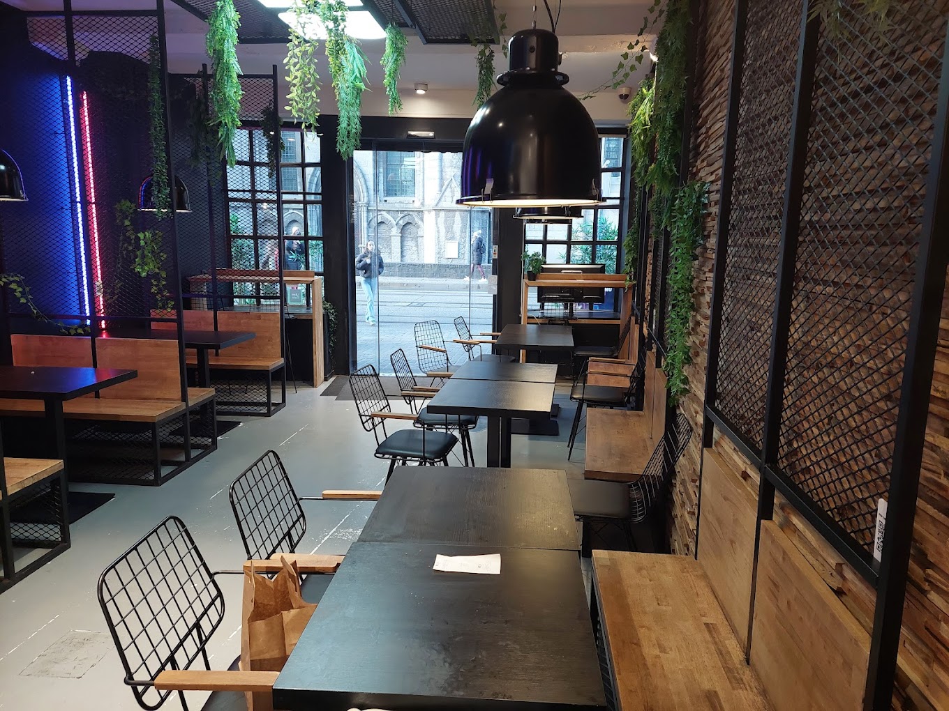 The interior of halal restaurant Nub Smashburger in Gent, Belgium, showing black tables, wooden benches, and hanging plants with a modern design.