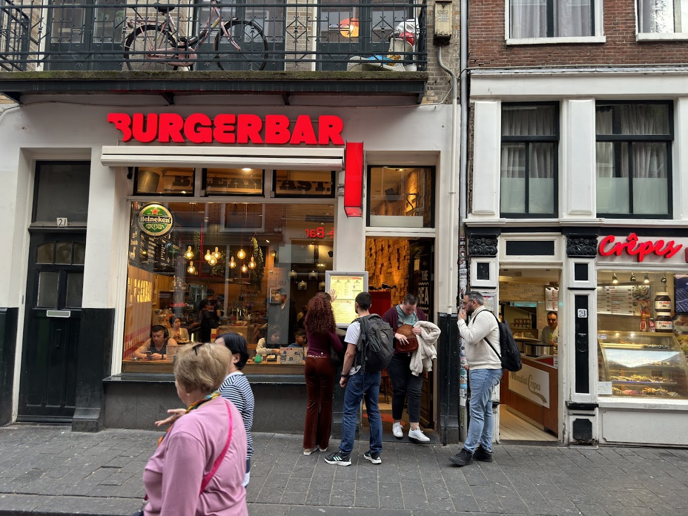 The exterior of halal restaurant Burger Bar in Amsterdam, Netherlands, showing a bright red sign with the name 'BURGERBAR' and a window displaying customers inside.