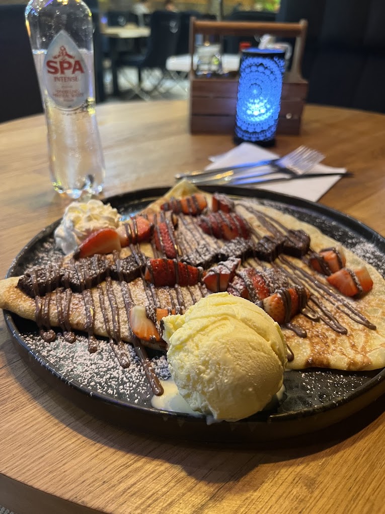 Une assiette de crêpes garnies de fraises, de sauce au chocolat et de crème fouettée, servies avec une boule de glace à la vanille au restaurant halal The Room à Anvers, Belgique.