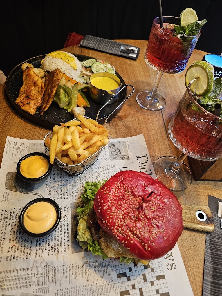 A colorful burger with a red sesame seed bun, lettuce, and a beef patty, served with fries and two sauces at The Room, a halal restaurant in Antwerpen, Belgium.