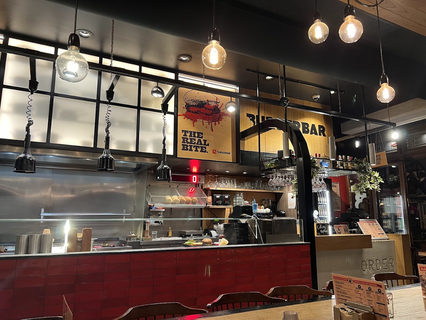 The interior of halal restaurant Burger Bar in Amsterdam, Netherlands, showing a modern kitchen setup with hanging lights, a red tiled counter, and a menu board.