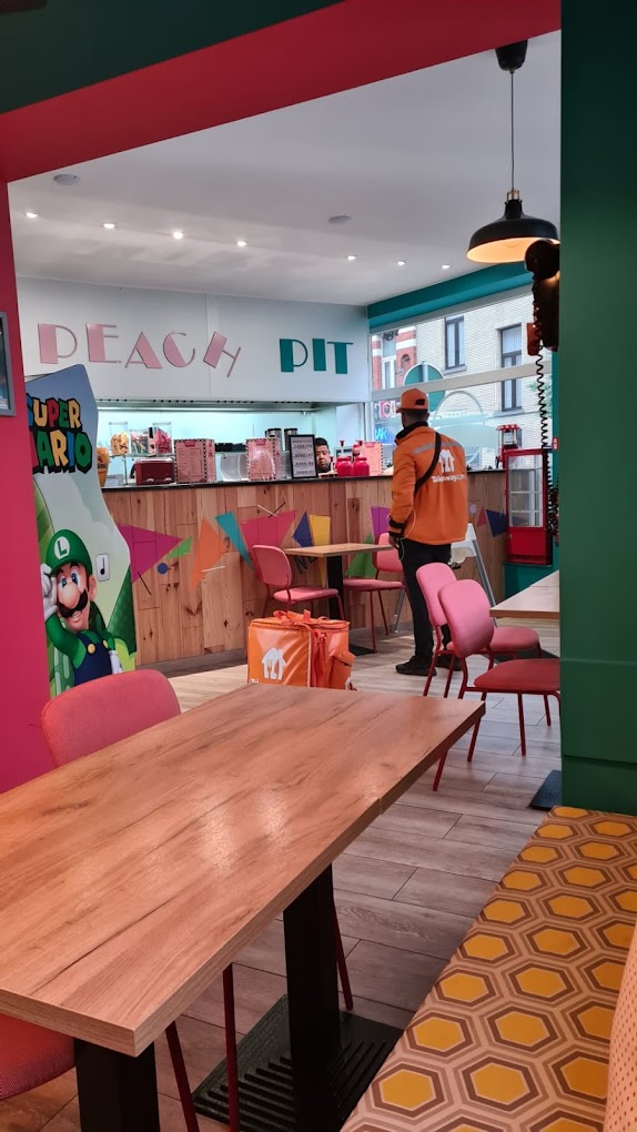 L'intérieur du restaurant halal Peach Pit à Schaerbeek, en Belgique, montrant une décoration colorée, des chaises roses et un comptoir avec un menu.