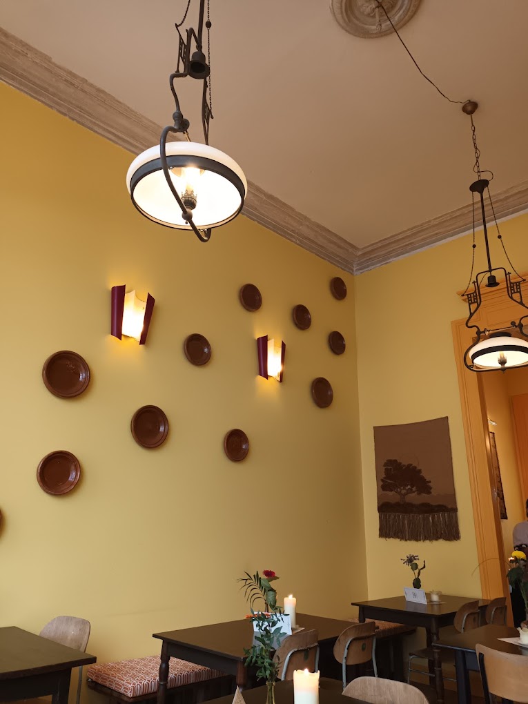 The interior of halal restaurant Lella in Antwerpen, Belgium, showing yellow walls adorned with decorative plates, pendant lights, and wooden tables with floral arrangements.