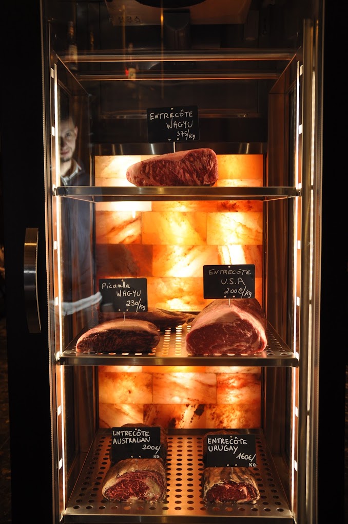 The interior of halal restaurant La Ruche in Bruxelles, Belgium, showing a display case with various cuts of meat, including Wagyu and Australian entrecôte, with price tags.