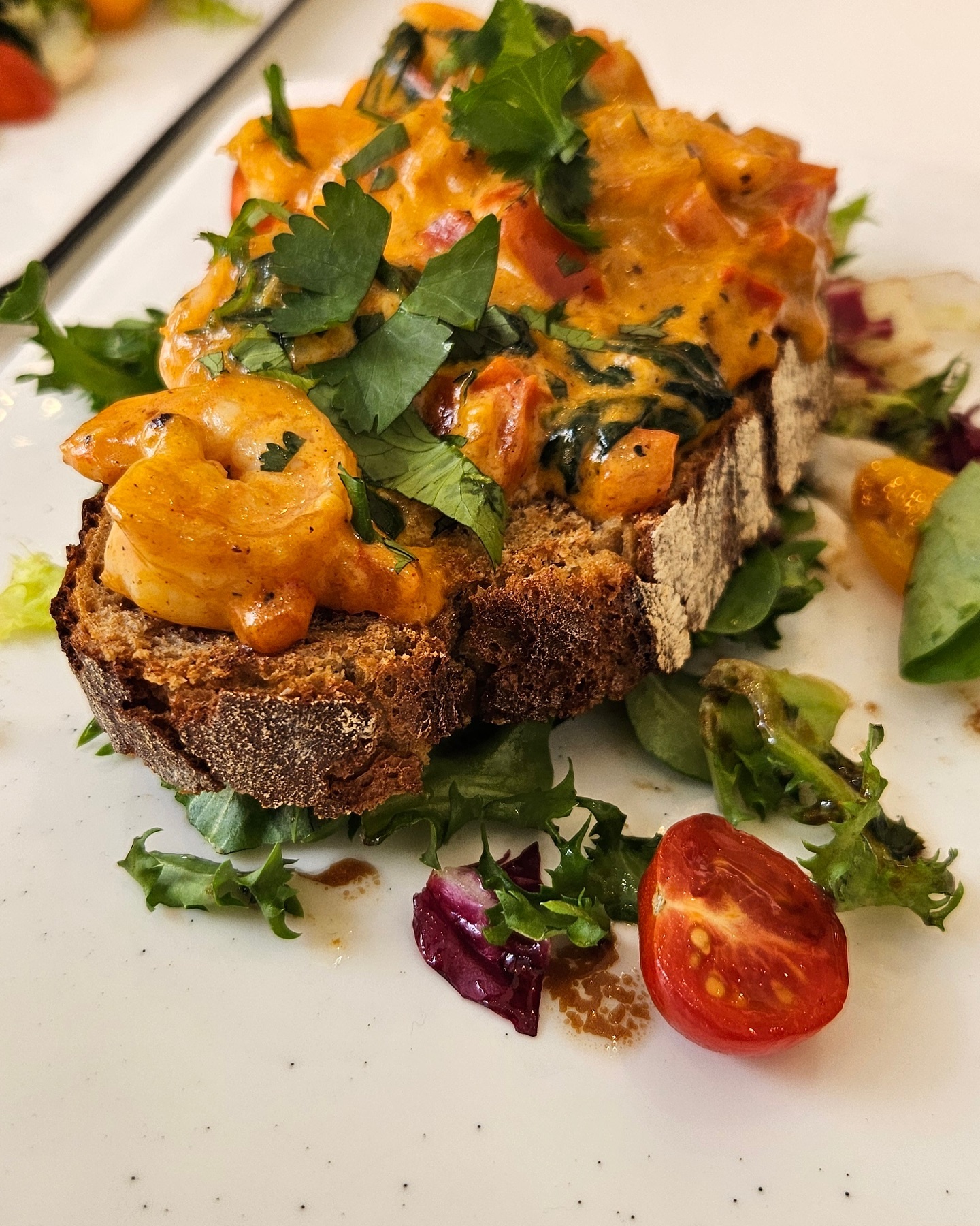 A slice of dark bread topped with shrimp in a creamy sauce, garnished with fresh herbs, served at 2D Café, a halal restaurant in Molenbeek-Saint-Jean, Belgium.