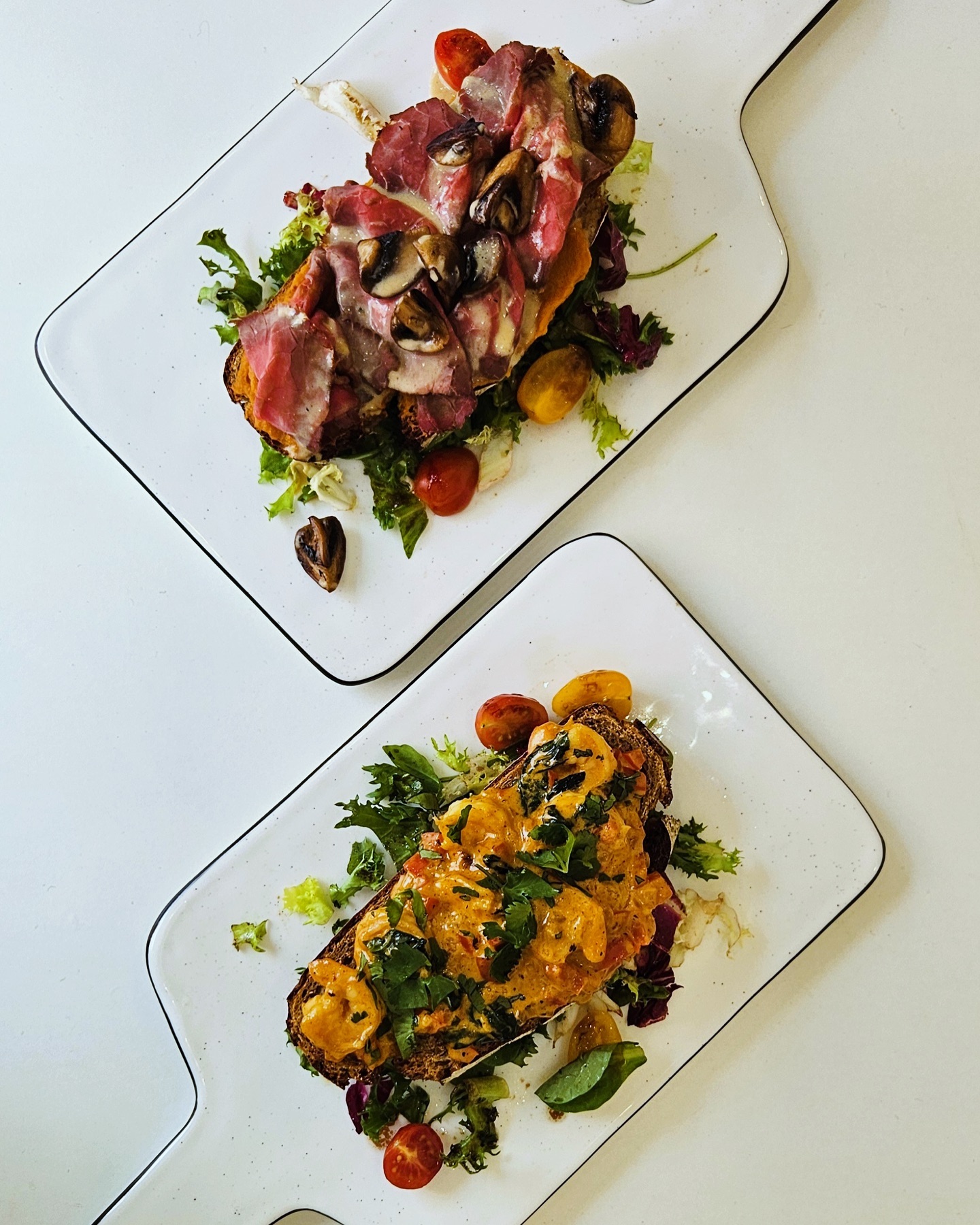 A dish featuring two pieces of toasted bread topped with sliced beef, mushrooms, and a colorful salad at 2D Café, a halal restaurant in Molenbeek-Saint-Jean, Belgium.