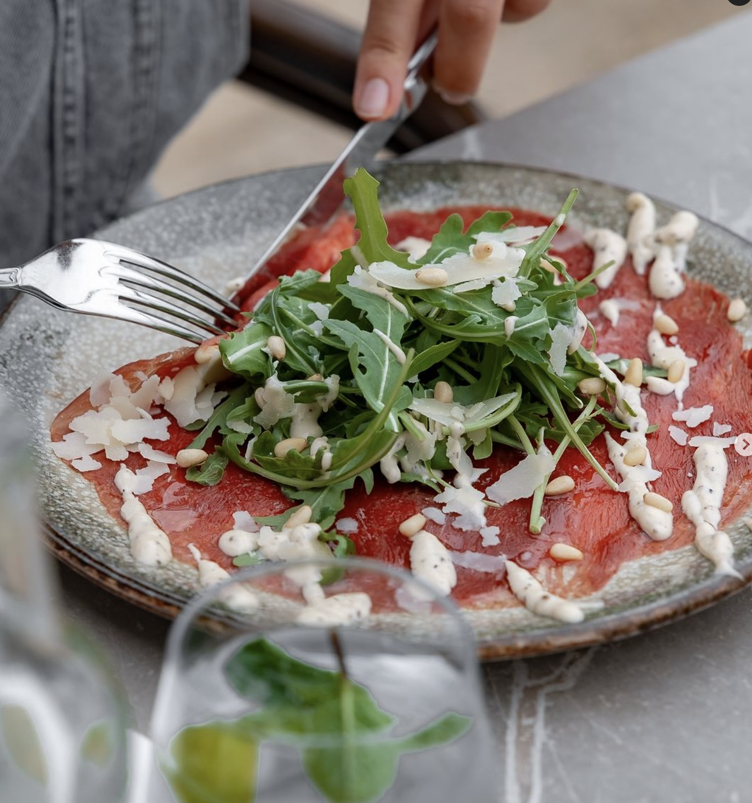 A plate of carpaccio topped with arugula, pine nuts, and drizzled with sauce at Mansion, a halal restaurant in Rotterdam, Netherlands.
