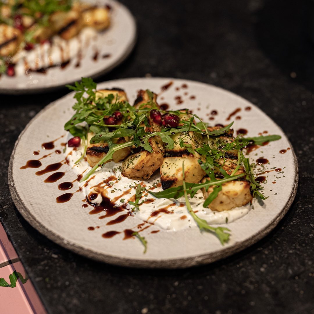 A plate of grilled halloumi cheese with arugula, pomegranate seeds, and a drizzle of balsamic reduction at Felfel, a halal restaurant in Antwerpen, Belgium.