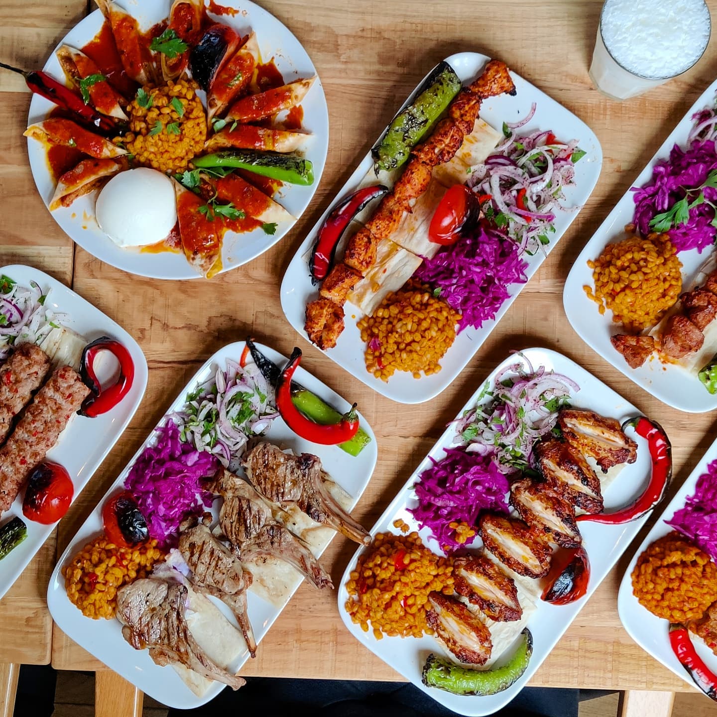 A variety of halal dishes are displayed on white plates at Ganii Kebap in Rotterdam, Netherlands. The dishes include grilled meats, rice, and vegetables.