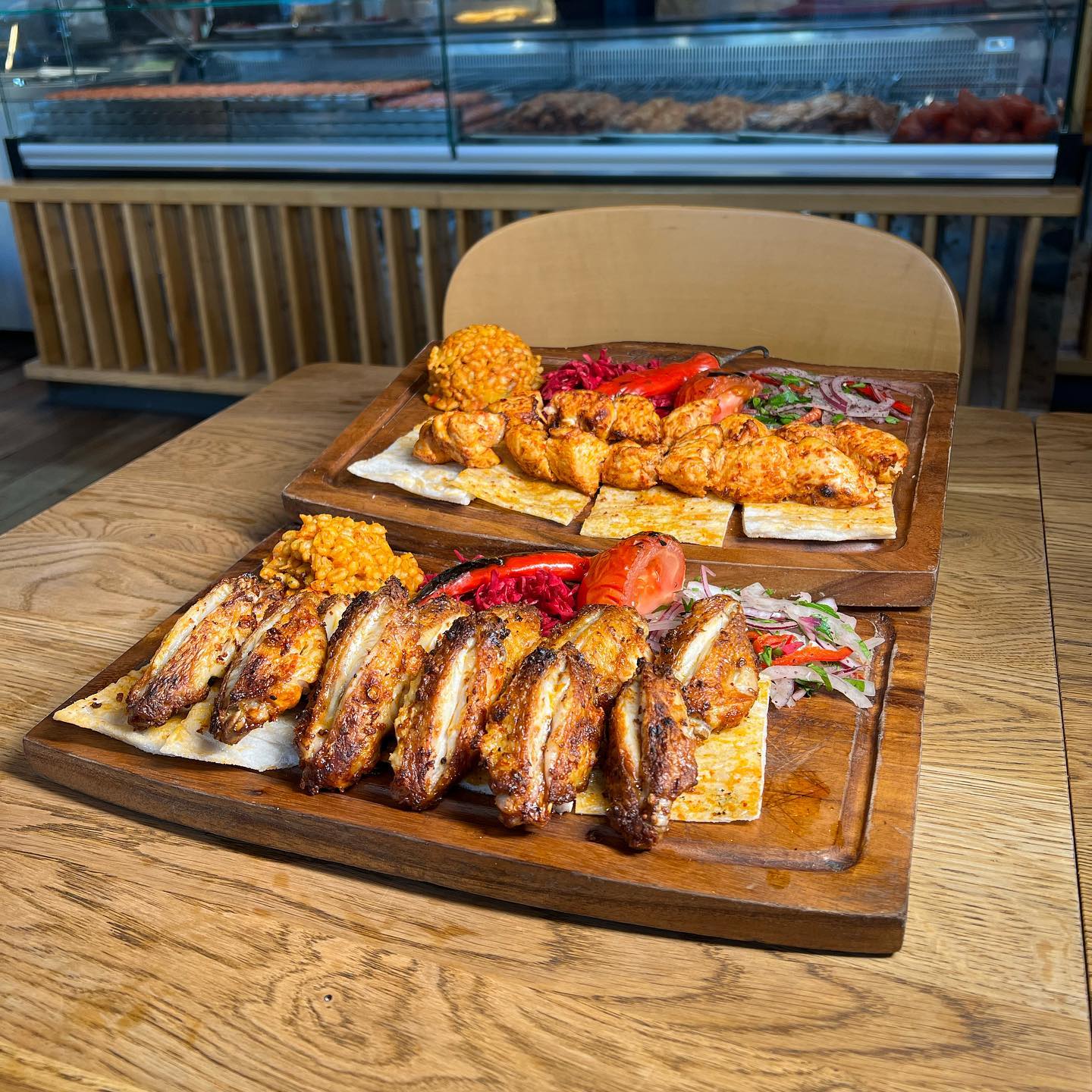 A close-up shot of a halal dish served on a wooden platter at Ganii Kebap in Rotterdam, Netherlands. The dish features grilled chicken wings, rice, and salad.