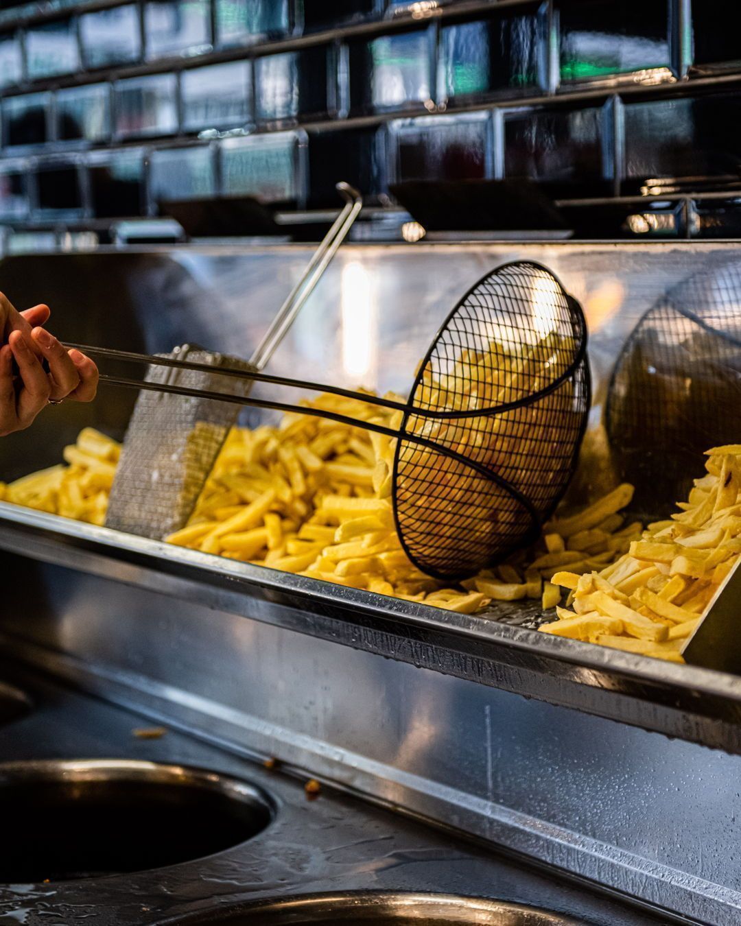 Het interieur van halal restaurant Snack Bosphorus in Oudergem, België, met een balie waarop een grote schaal met versgebakken frietjes staat en een medewerker die een schuimspaan gebruikt om ze te serveren.