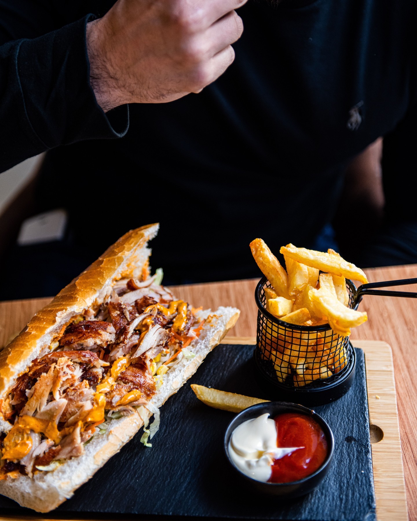 Een sandwich gevuld met gegrilde kip, sla en sauzen, geserveerd met frietjes en dipsauzen bij Snack Bosphorus, een halal restaurant in Oudergem, België.