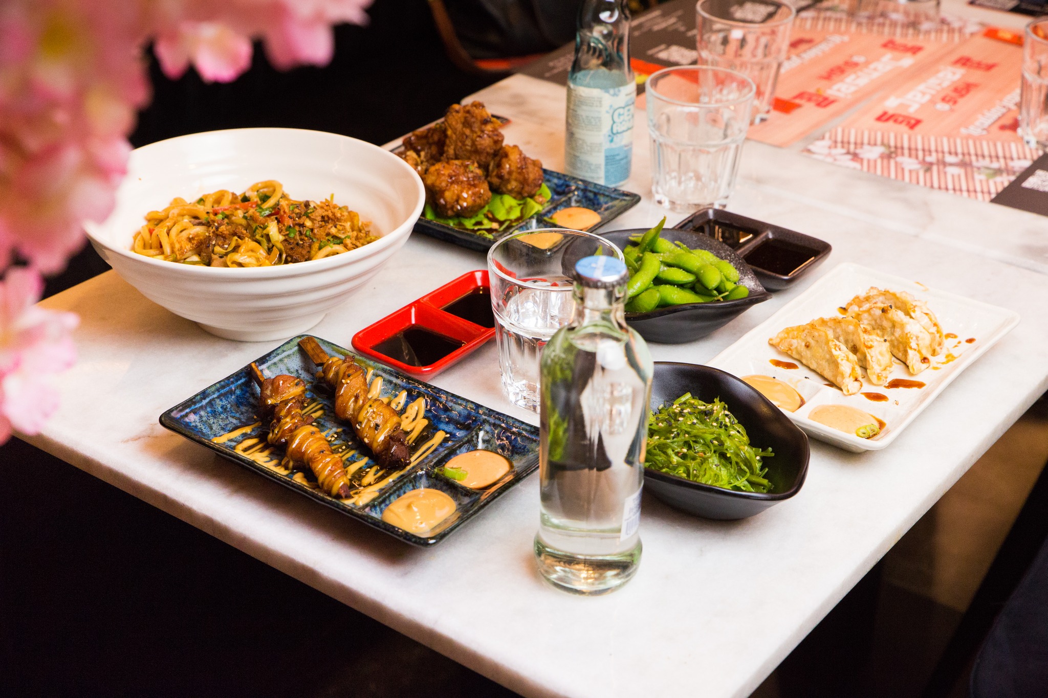 A variety of dishes including noodles, skewers, edamame, and dumplings at Sensei Sushi, a halal restaurant in Schaerbeek, Belgium.