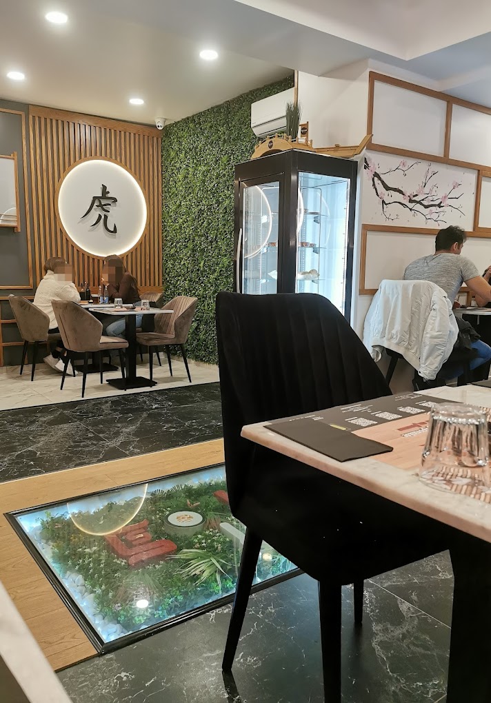The interior of halal restaurant Sensei Sushi in Schaerbeek, Belgium, showing a modern design with green wall decor, wooden accents, and a glass display cabinet.