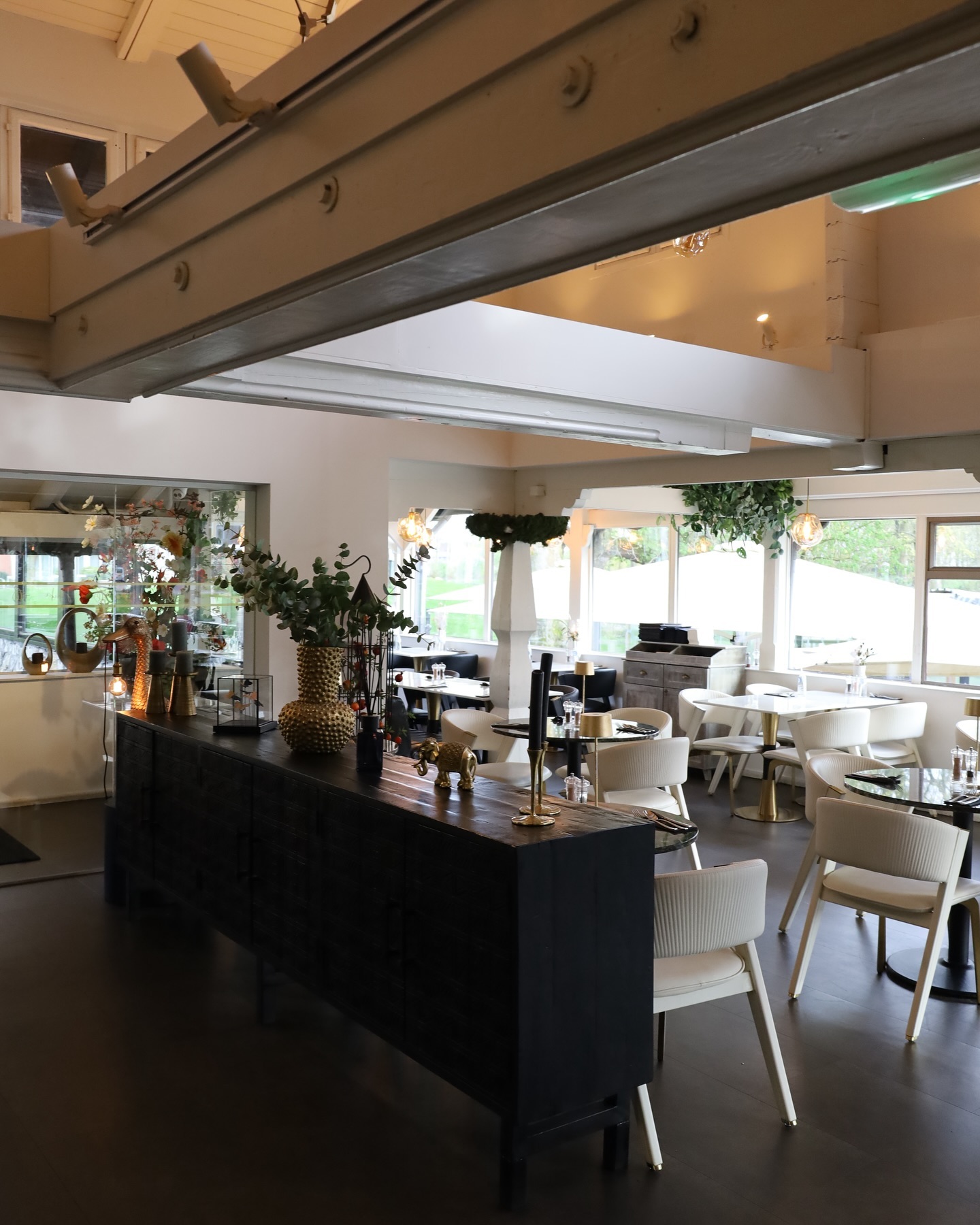 L'intérieur de Hkiki à Rotterdam, aux Pays-Bas, montrant une salle à manger moderne avec des chaises blanches, des tables en bois et des plantes décoratives.