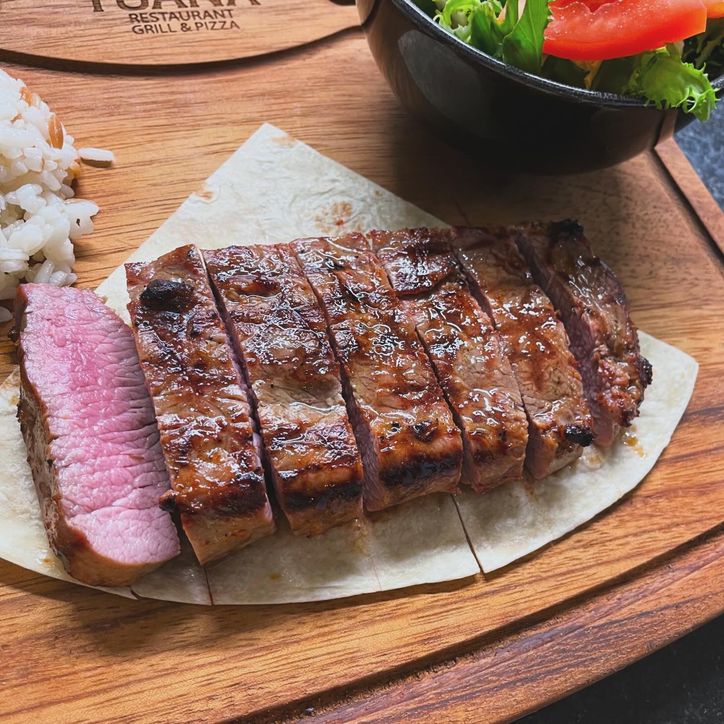 A grilled steak with a pink center, served with rice and a side salad at Tuana, a halal restaurant in Sint-Niklaas, Belgium.
