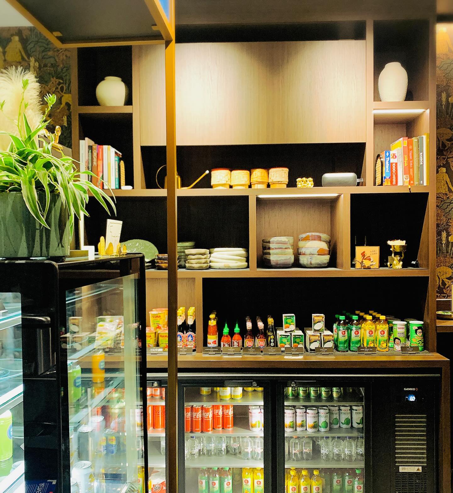 The interior of halal restaurant Aari Thai in Antwerpen, Belgium, showing shelves with various products, a plant, and a refrigerator filled with drinks.