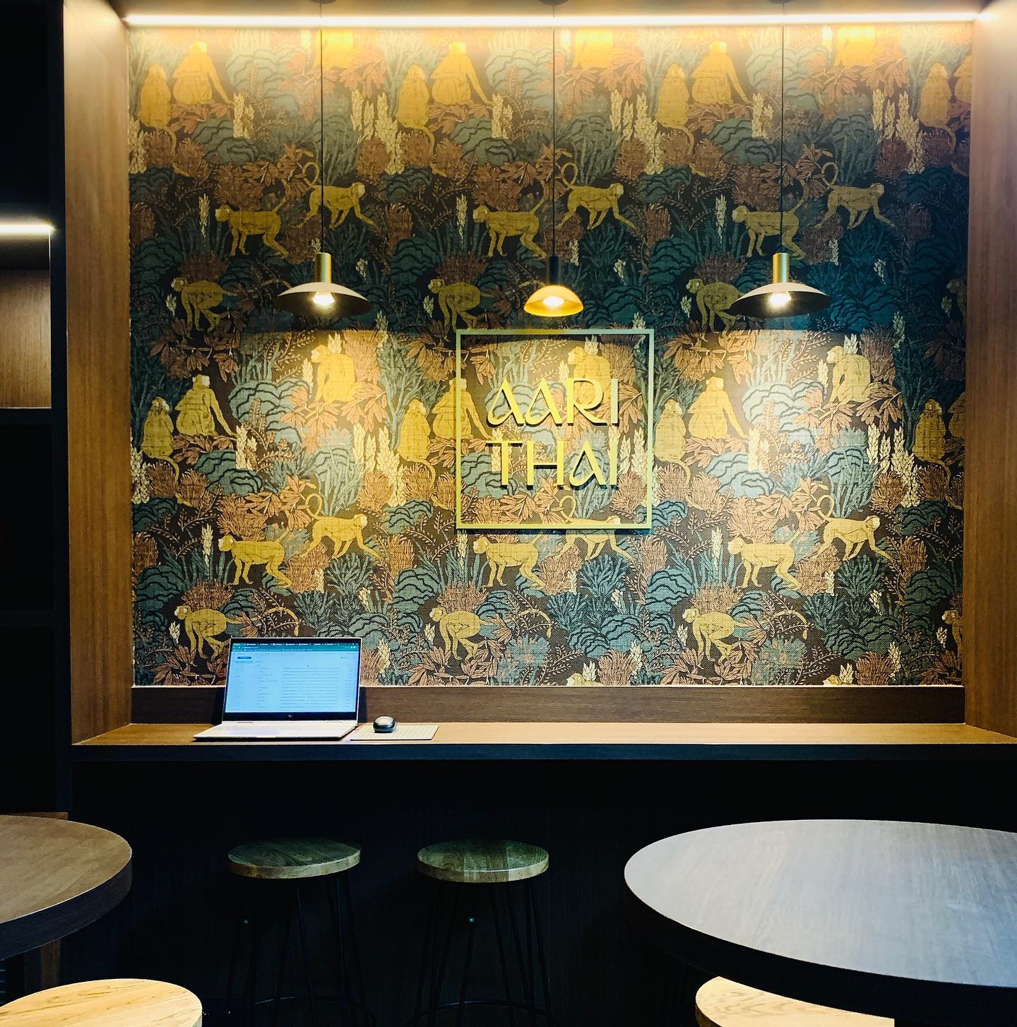 The interior of halal restaurant Aari Thai in Antwerpen, Belgium, showing a decorative wall with golden patterns, pendant lights, and a wooden counter with stools and a laptop.