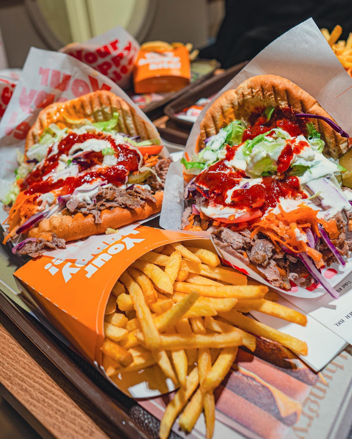 Une assiette de deux sandwiches pita garnis de viande effilochée, de laitue, de carottes et de sauces, accompagnée d'une portion de frites au restaurant halal Plaset Doner Burger à Ixelles, Belgique.