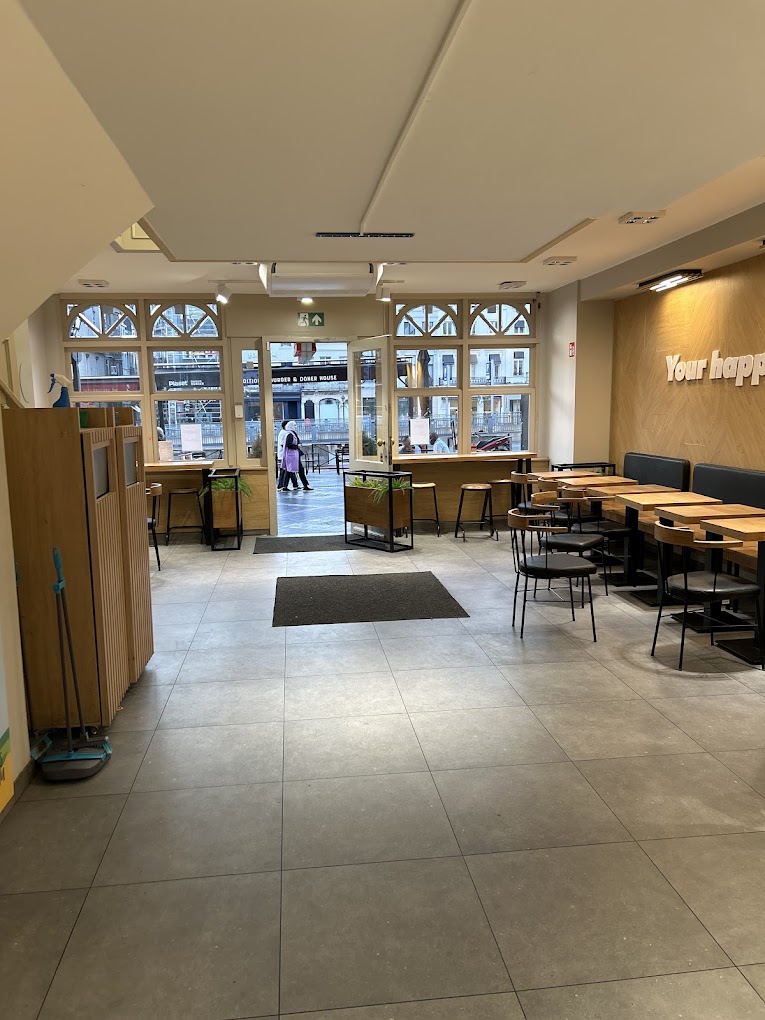 L'intérieur du restaurant halal Plaset Doner Burger à Ixelles, en Belgique, montrant un espace de restauration spacieux avec des tables et des chaises en bois, de grandes fenêtres et une atmosphère accueillante.