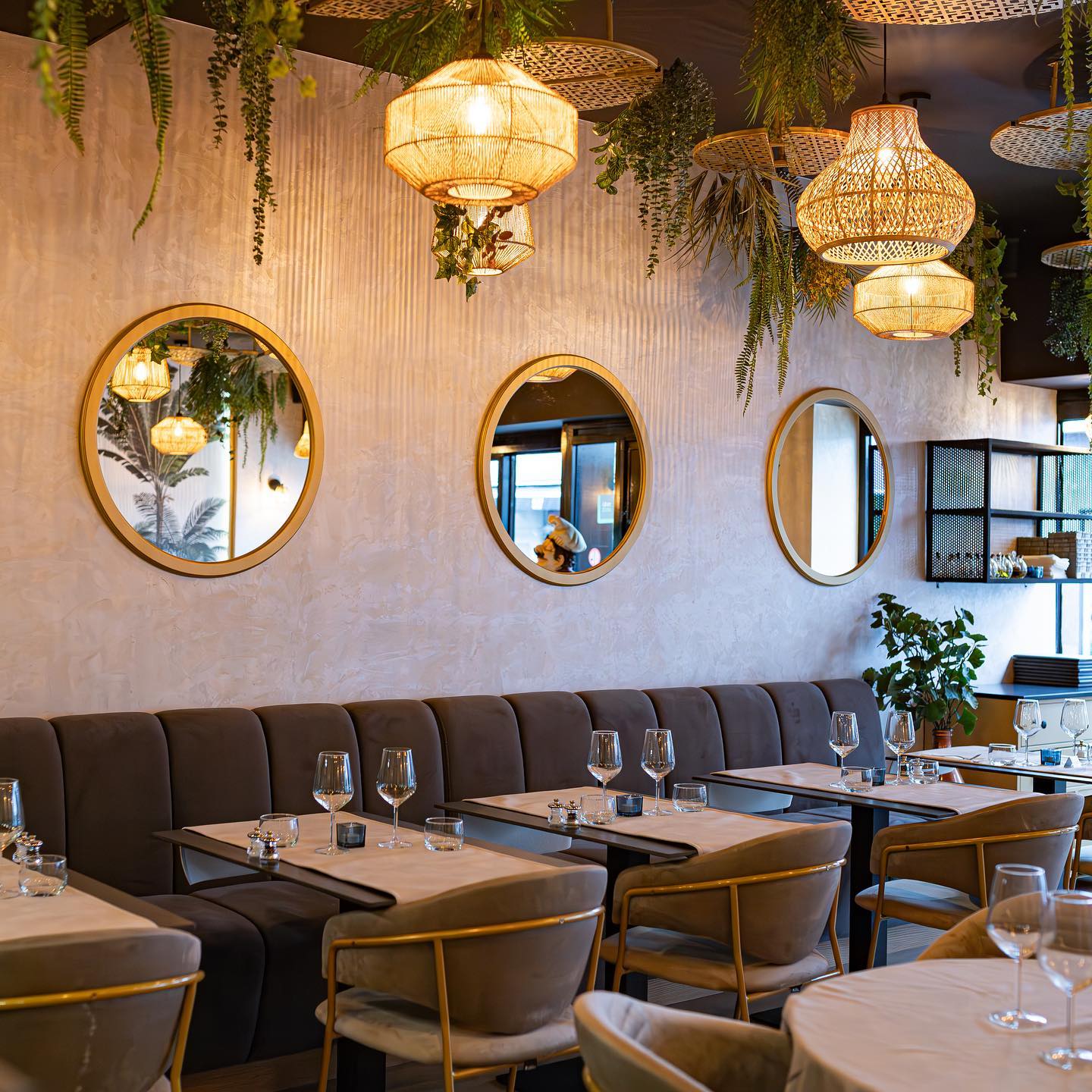 Het interieur van halal restaurant The Manzoni in Brussel, België, met elegante verlichting, ronde spiegels en een gezellige zithoek met gedekte tafels.