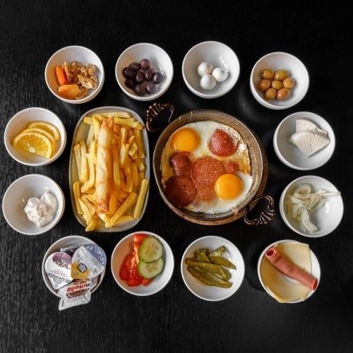 Un petit-déjeuner composé d'œufs au plat, de saucisses et de frites, accompagné de divers petits bols d'olives, de fruits et de condiments au restaurant halal The Cousins à Bruxelles, Belgique.