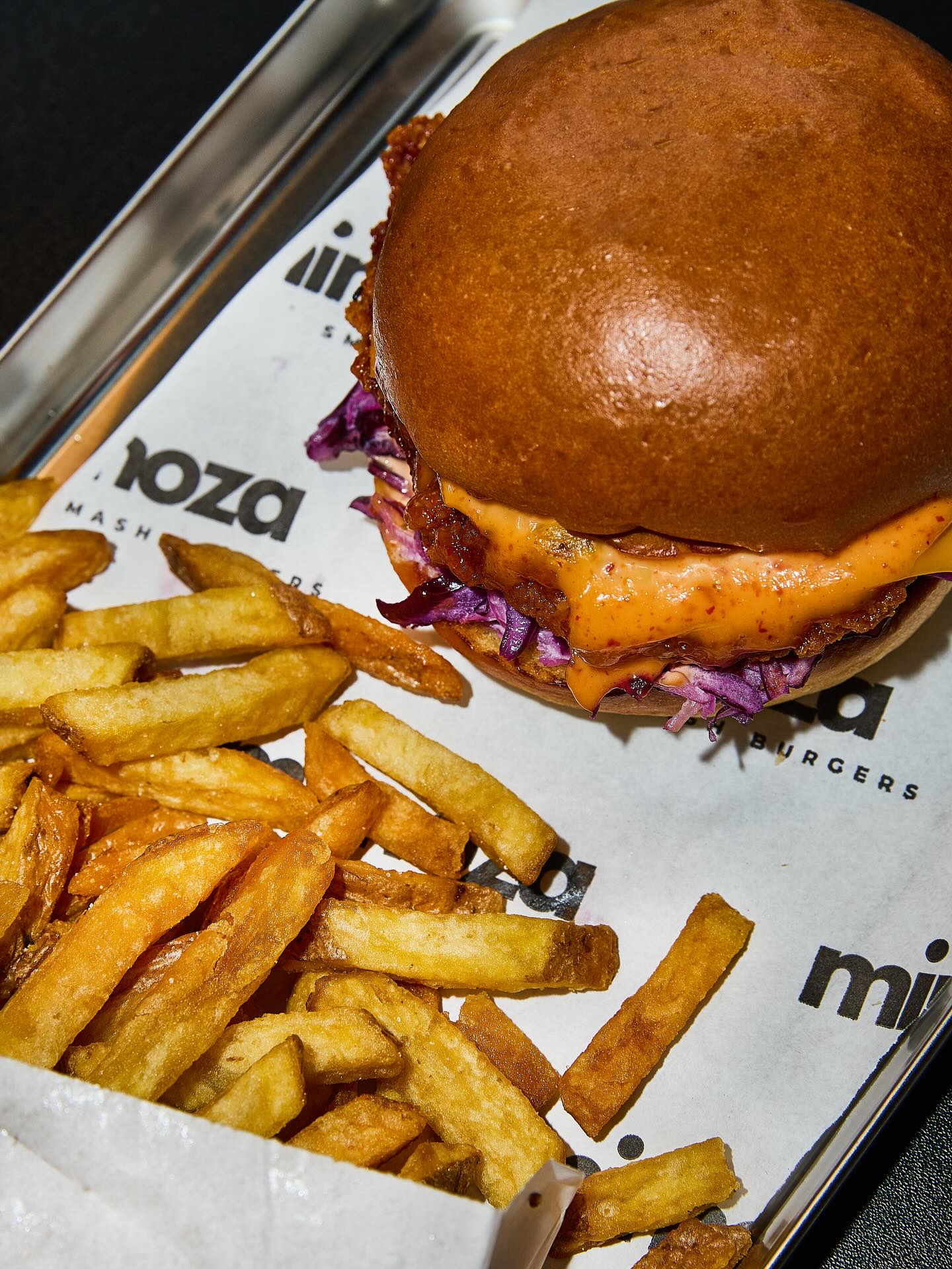 A burger with coleslaw and sauce, accompanied by fries, at Mimoza Smashburgers, a halal restaurant in Rotterdam, Netherlands.