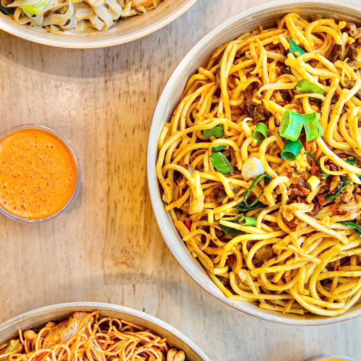 A bowl of stir-fried noodles with green onions and a side of orange sauce at YouWok, a halal restaurant in Wijnegem, Belgium.