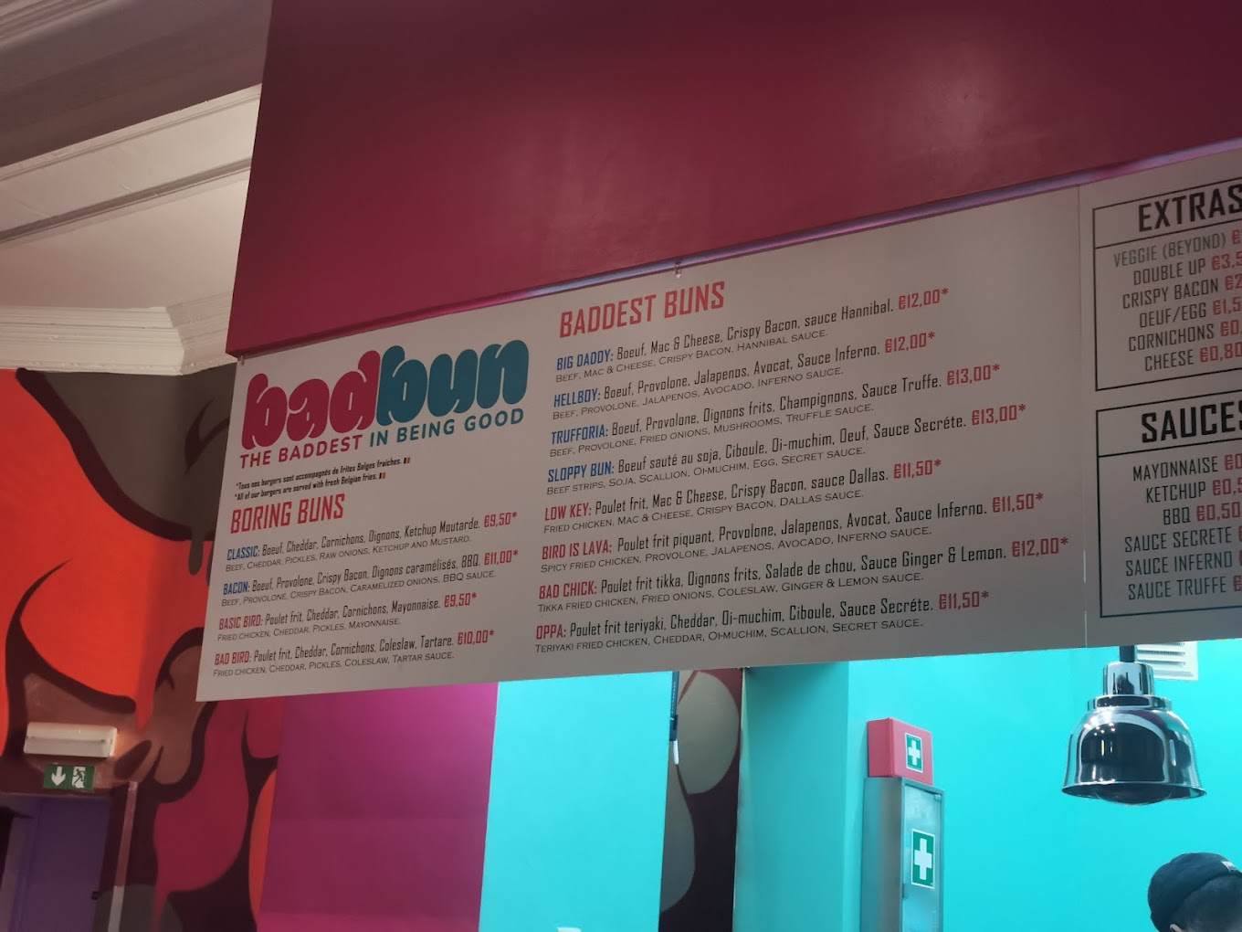 The interior of halal restaurant Bad Bun in Ixelles, Belgium, showing a colorful menu board with various burger options and prices.