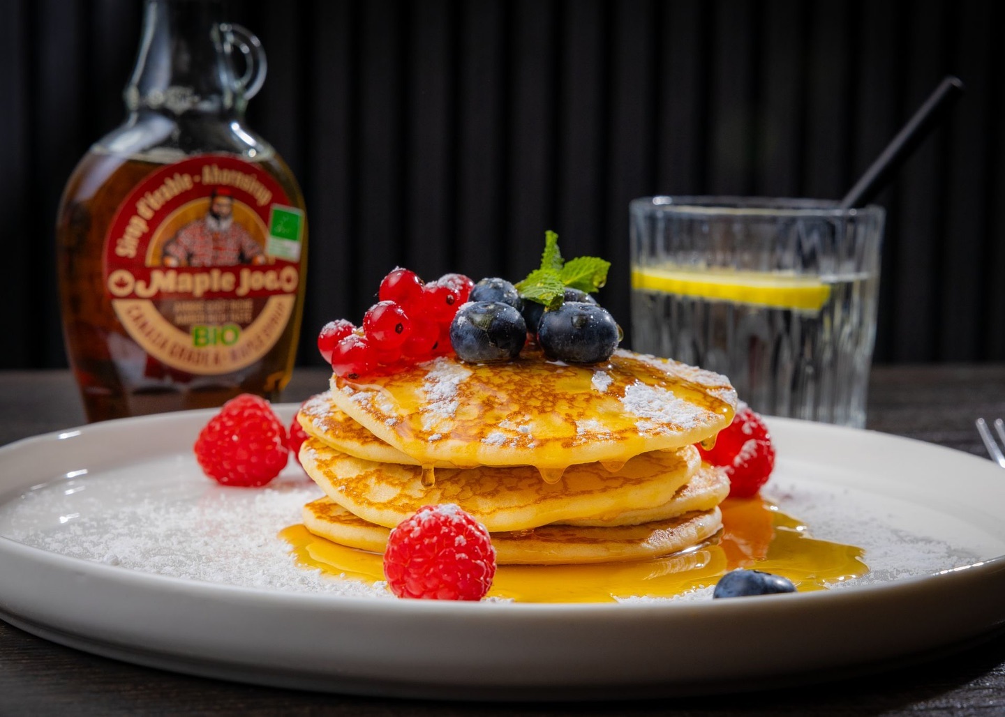 A stack of pancakes topped with blueberries, raspberries, and red currants, drizzled with maple syrup, at La Ruche, a halal restaurant in Eindhoven, Netherlands.