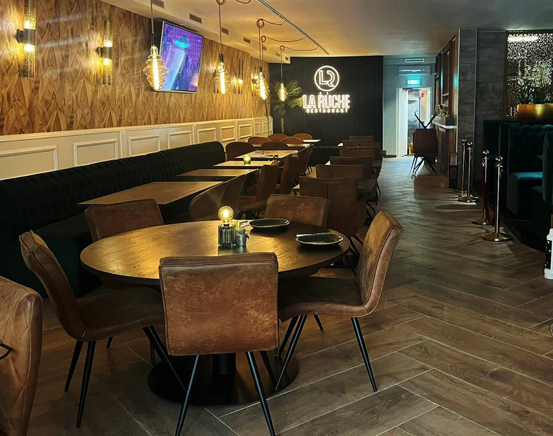 The interior of halal restaurant La Ruche in Eindhoven, Netherlands, showing wooden walls, round tables, brown leather chairs, and decorative lighting.