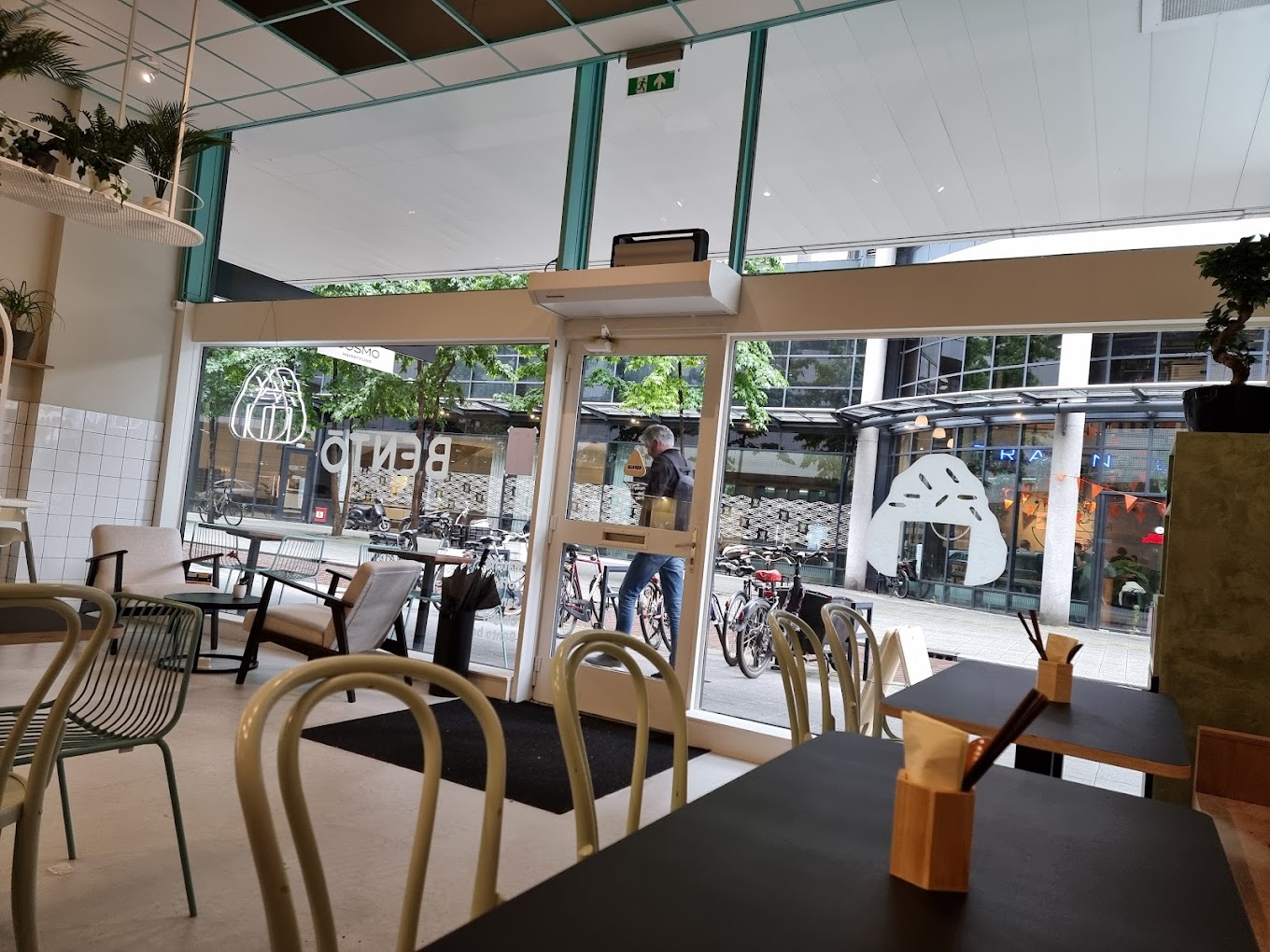 The interior of halal restaurant Bento Café in Rotterdam, Netherlands, showing a modern design with light-colored furniture, large windows, and a view of bicycles outside.