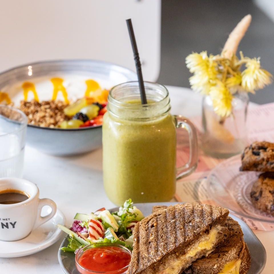 A green smoothie, a sandwich with melted cheese, a side salad, a cup of coffee, and a bowl of yogurt with granola and fruit at Koffie Met Tony, a halal restaurant in Ede, Netherlands.