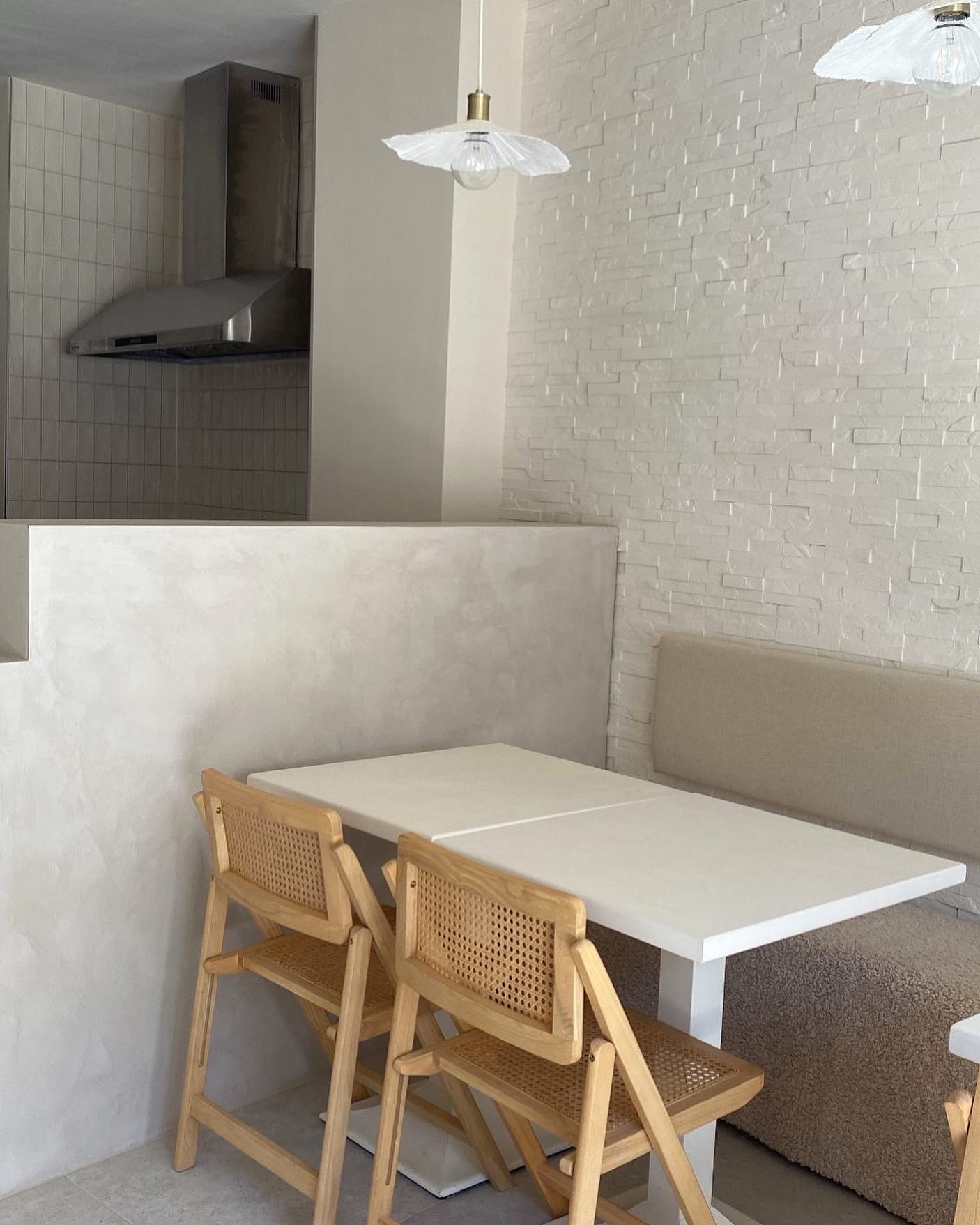 The interior of halal restaurant The Bread Bar in Gent, Belgium, showing a minimalist design with a white stone wall, wooden chairs, and a simple table setup.