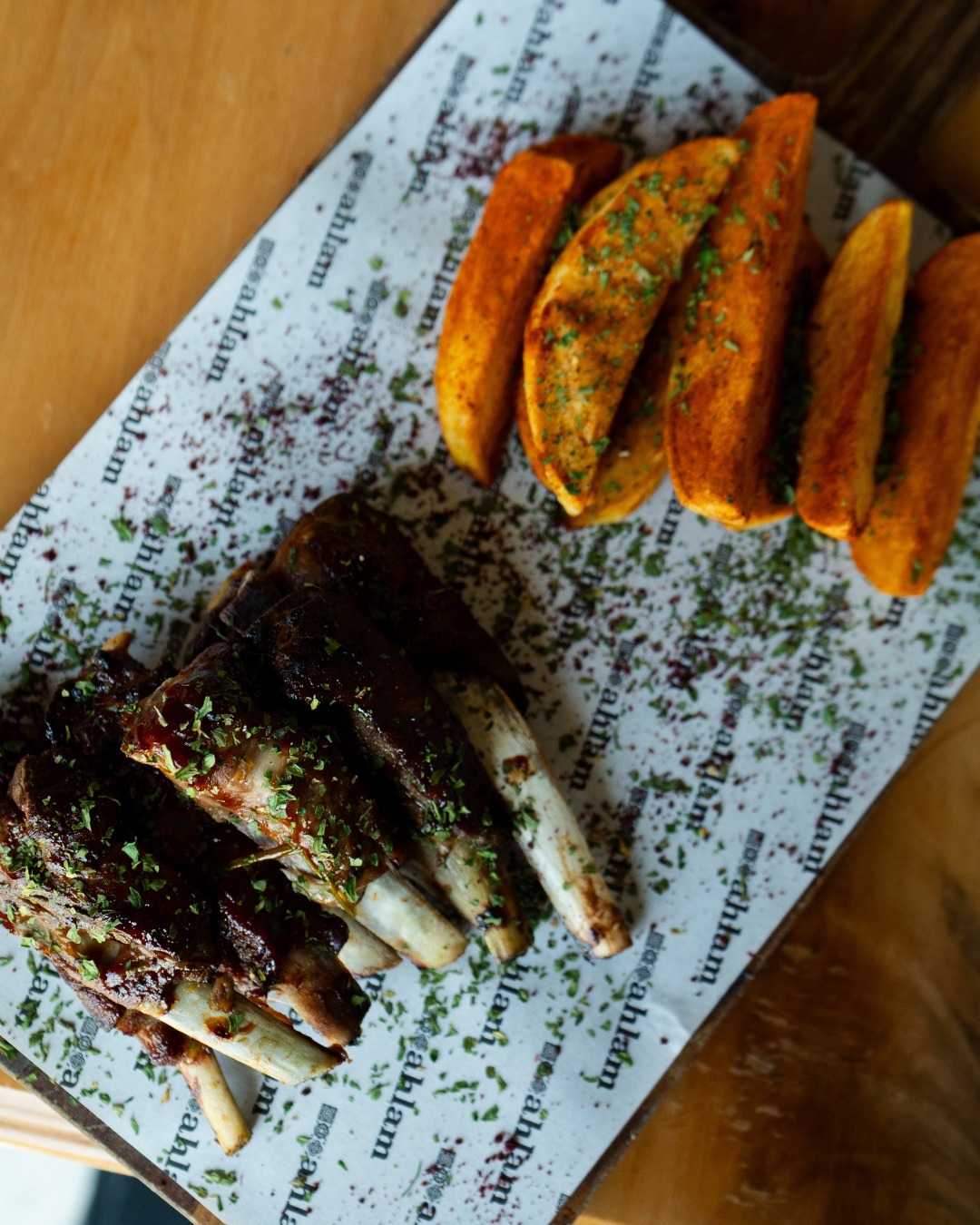 A plate of grilled lamb ribs with herbs and seasoned potato wedges at Restaurant Ahlam, a halal restaurant in Den Haag, Netherlands.