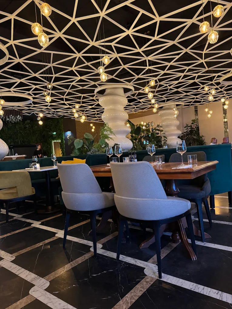 The interior of halal restaurant Restaurant Ahlam in Den Haag, Netherlands, showing a modern design with a geometric ceiling, hanging lights, and green plants.