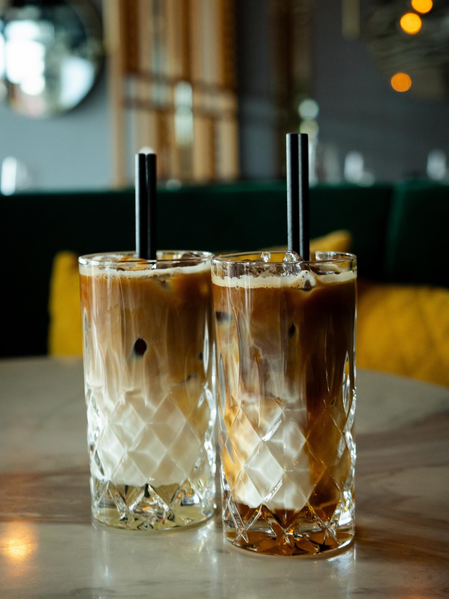 Two glasses of iced coffee with cream and ice on a marble table at a restaurant.