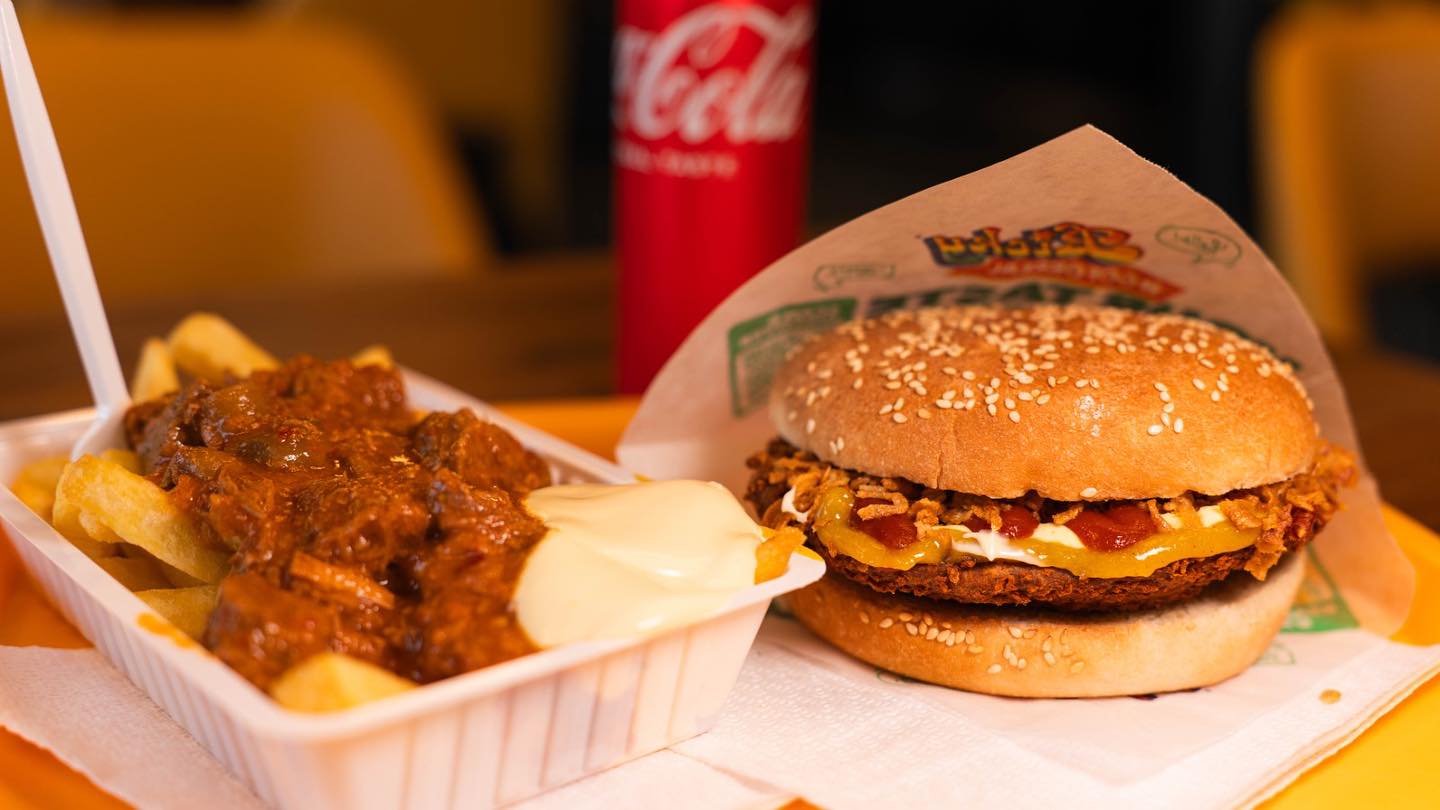 A sesame seed bun with fried chicken, cheese, and sauces, accompanied by fries topped with a meat sauce at City Food Lounge, a halal restaurant in Genk, Belgium.