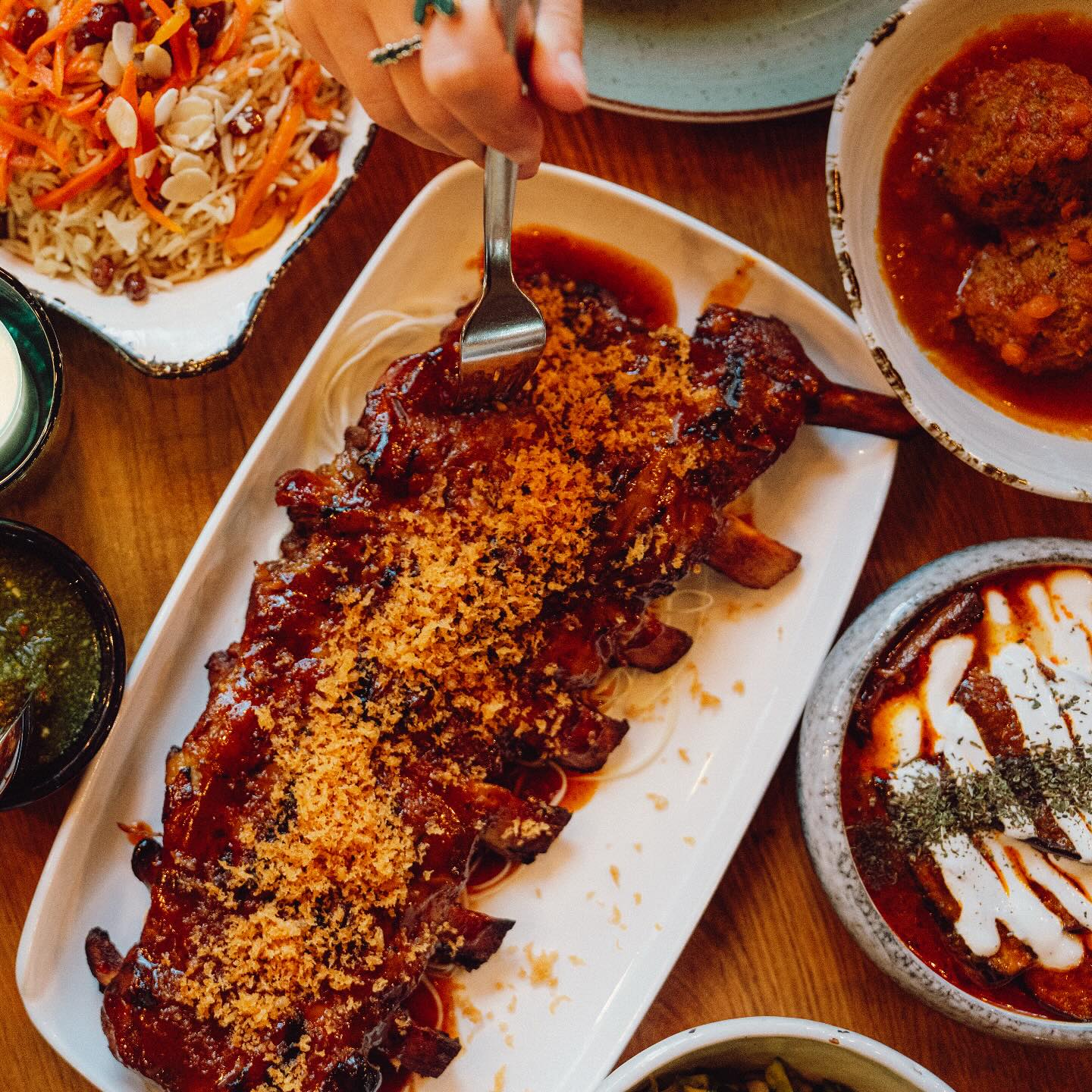 A plate of glazed ribs topped with crispy onions, served with sides of salad, sauce, and meatballs at Kite, a halal restaurant in Rotterdam, Netherlands.