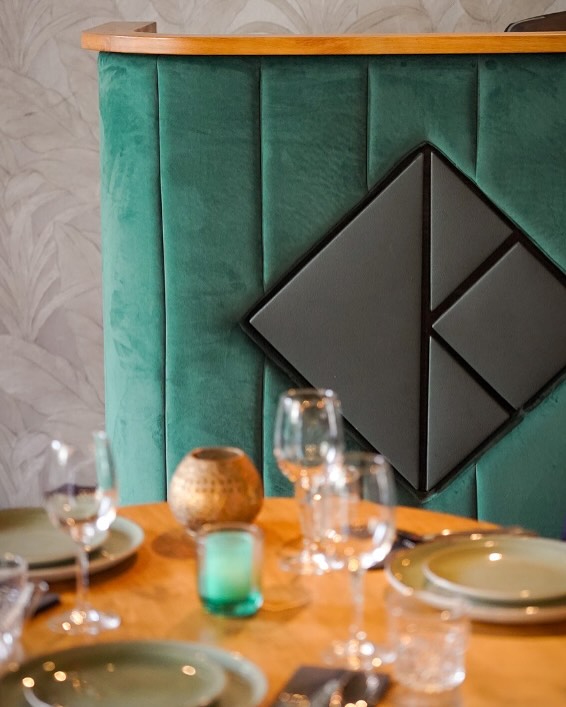 The interior of halal restaurant Kite in Rotterdam, Netherlands, showing a green upholstered booth with a geometric design and a wooden table set with plates and glasses.
