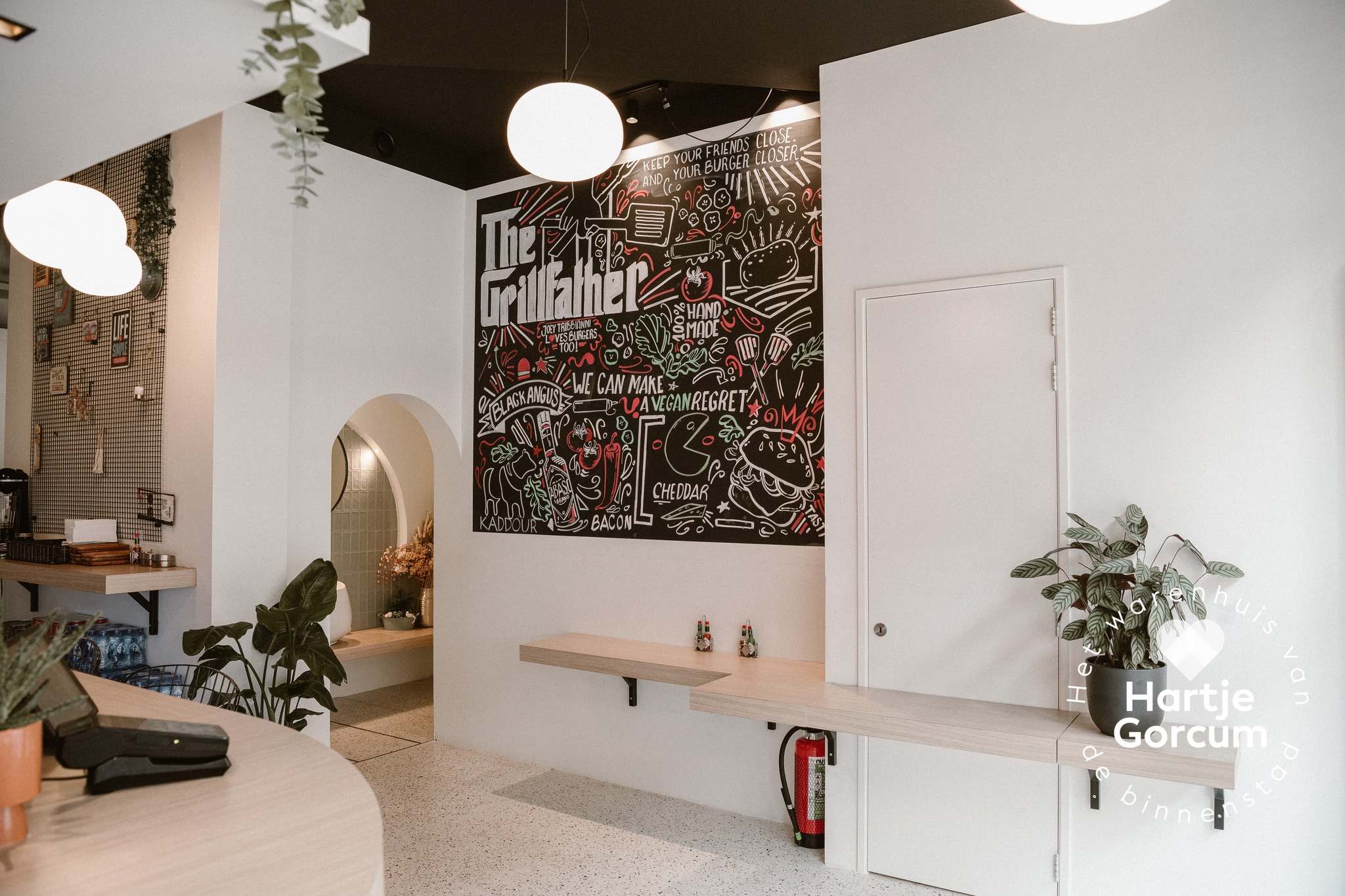 The interior of halal restaurant Just Burgers in Gorinchem, Netherlands, showing a colorful mural with burger-themed illustrations, a wooden counter, and plants.